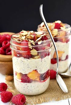 two jars filled with fruit and yogurt on top of a table next to raspberries