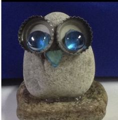 an owl figurine with large blue eyes on a stone base in front of a blue background