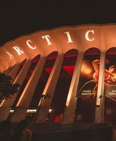 the entrance to an arena at night with lights on and people walking around outside it