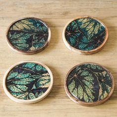 four wooden buttons with green leaves on them sitting on a table next to each other