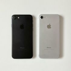 two iphones sitting next to each other on a white surface, one is black and the other is silver