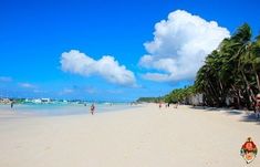 people are walking on the beach near some palm trees and boats in the water behind them