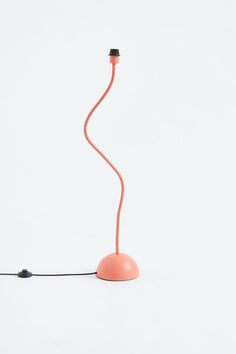 a pink lamp on a white surface with a black cord attached to the light bulb