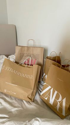 two brown paper bags sitting on top of a bed next to each other with the word zara printed on them