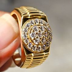 a close up of a person holding a gold ring with white diamonds on the side