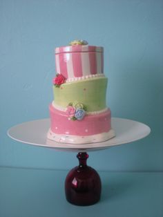 a three tiered cake sitting on top of a white plate next to a red vase