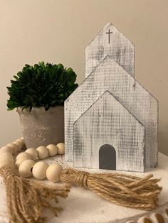 a small white wooden church sitting on top of a table next to a potted plant