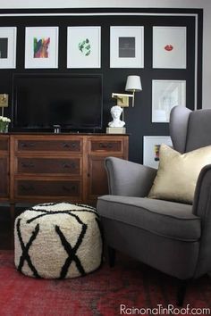 a living room with black walls and pictures on the wall, a gray chair and footstool