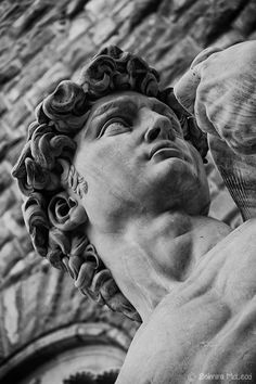 a black and white photo of a statue in front of a stone building with a clock on it's face