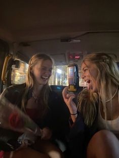 two young women sitting in the back of a car talking on their cell phones and laughing