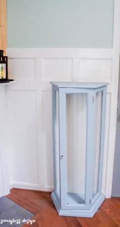 a corner cabinet in the corner of a room with wood flooring and white walls