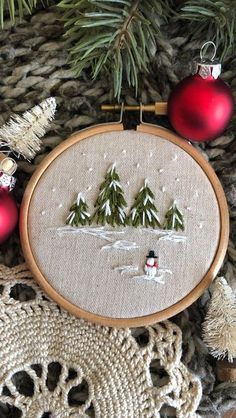 a cross stitch christmas ornament hanging on a tree branch with ornaments around it