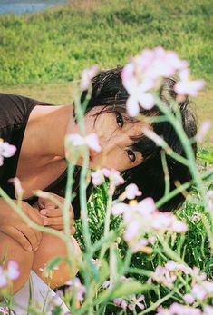 a woman kneeling down in the grass with pink flowers around her and looking at something