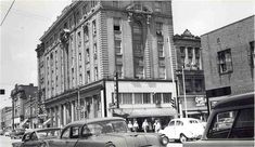 an old black and white photo of cars parked on the street in front of buildings