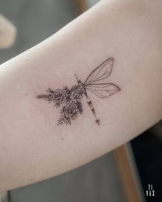 a dragonfly tattoo on the arm with flowers in it's wings and an arrow