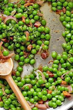 peas and onions are being cooked in a pot with a wooden spoon on the side