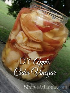 a jar filled with sliced apples sitting on top of a wooden table next to a tree