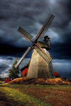 a windmill sitting in the middle of a field under a cloudy sky with dark clouds