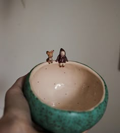 two tiny figurines sitting on top of a green bowl in someone's hand