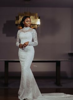 a woman standing in front of a table wearing a white dress with sheer lace sleeves