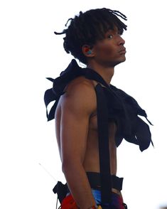 a man with dreadlocks standing in front of a white background wearing a black top