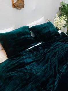 a bed with green blankets and pillows in a room next to a vase filled with flowers