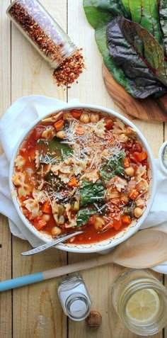 a white bowl filled with pasta and spinach on top of a wooden cutting board