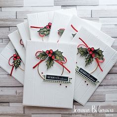 four christmas cards with holly and ribbons on them, sitting on a wooden table top