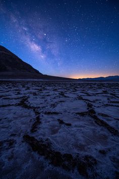 the night sky is filled with stars above a barren area, and there are footprints in the sand