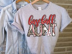 Show how proud you are of your baseball player with this cute shirt! * All shirts and sweaters are unisex fit. You can find a size and color chart in the extra photos of this listing. * Softstyle Tees - 4.5 oz. weight, 100% preshrunk cotton * Heavy Blend Sweaters - 8 oz. weight, 50% cotton, 50% polyester * This design is applied to the shirt using a DTF Transfer and heat press. * The standard shipping for this order is via USPS First Class mail. CARE INSTRUCTIONS: * Machine wash inside out, cold, gentle * Tumble dry low or hang dry * Do no iron directly on image Please note that I try my best to represent the true colors of my work but all screens show in a slightly different lighting.  All items are made in my smoke-free home! Baseball Aunt, Baseball Letters, Aunt Shirt, Aunt Shirts, Sports Shirt, Cute Shirt, Letter T, Baseball Players, Sports Shirts