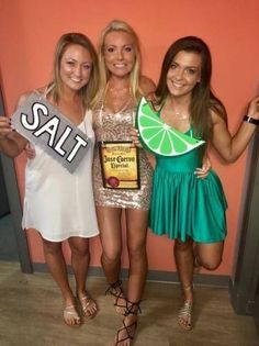 three beautiful young women standing next to each other in front of a pink wall holding up signs