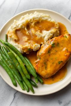 chicken with gravy, mashed potatoes and green beans on a white plate