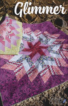 a pink and green quilt on the ground next to some rocks with leaves around it