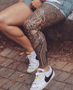 a woman sitting on the ground with her legs crossed and tattoos on her leg,