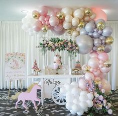 a table topped with lots of balloons next to a unicorn cake and other decorations on top of it