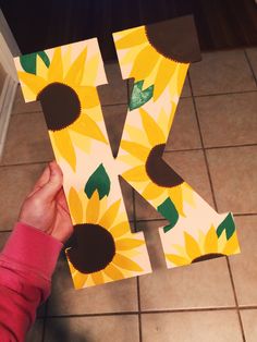 someone is holding up the letter k made out of paper sunflowers and green leaves