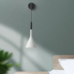 a white lamp hanging from the side of a wall next to a bed and potted plant