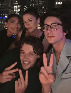 four people posing for the camera in front of a cityscape at night with their fingers up