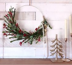 a christmas wreath with red berries and greenery hangs on a wall next to candles