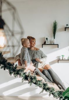 mother and daughter sitting on stairs with christmas garland in the foreground, smiling at each other