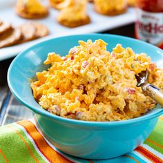 a blue bowl filled with food on top of a colorful table cloth next to crackers