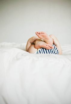 a baby laying on top of a white bed with his feet tucked under the covers