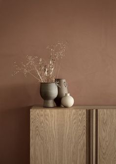 two vases sitting on top of a wooden cabinet in front of a pink wall