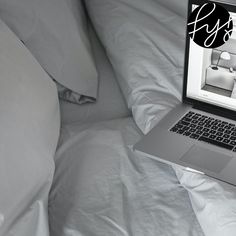 an open laptop computer sitting on top of a bed covered in white sheets and pillows