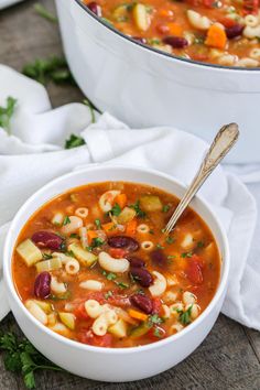 a white bowl filled with pasta soup next to a pot full of other food on a table