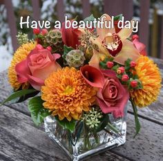 a vase filled with orange and yellow flowers on top of a wooden table in the snow