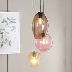 three different colored glass lights hanging from a light fixture in a room with pictures on the wall