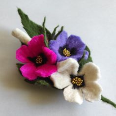 three different colored flowers are sitting on a white table top, one is purple and the other is pink