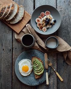 an egg and sliced avocado are on a plate next to bread, butter, and coffee