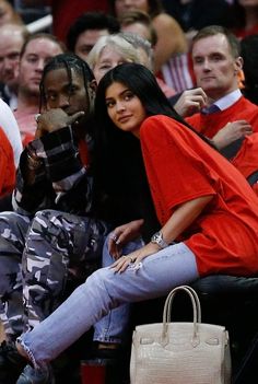 two women sitting on the sidelines at a basketball game, one holding a purse